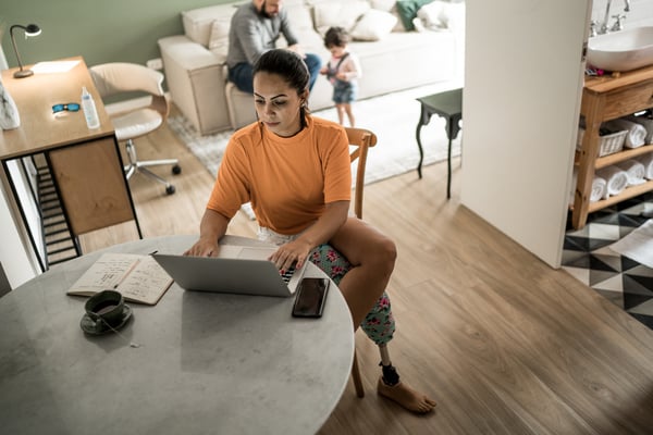 Person with prosthetic leg using laptop working at home with family in background