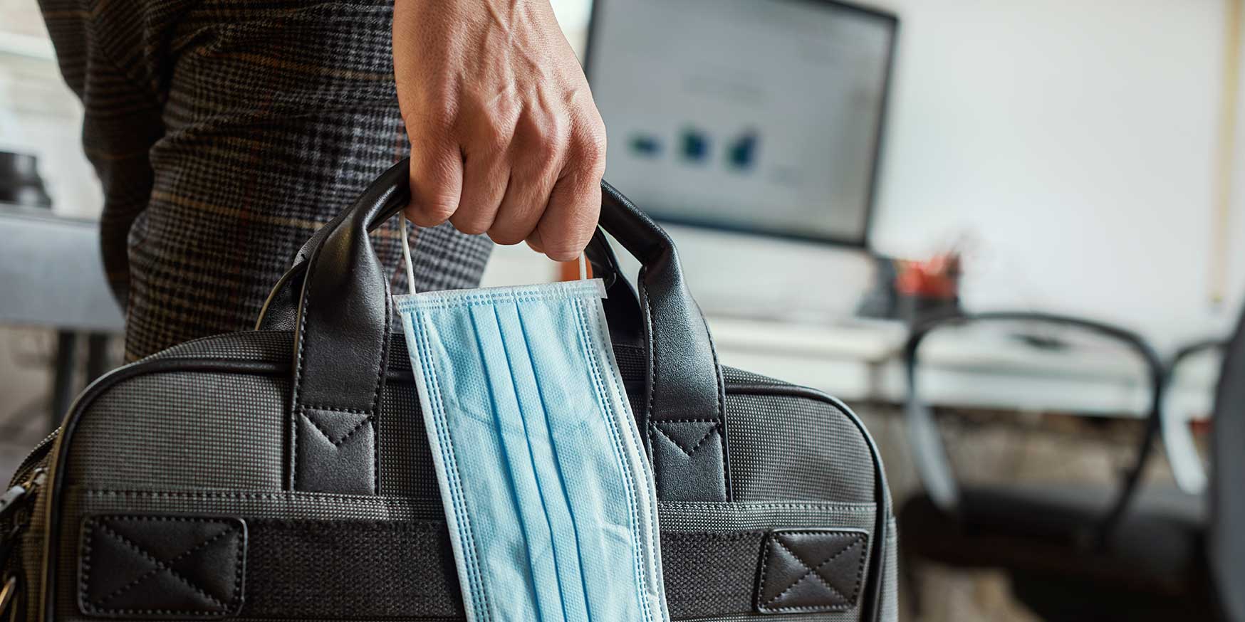 Person with a briefcase and a surgical mask returning to the office